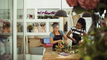 Two women in a flower shop making a bouquet of flowers together and smiling
